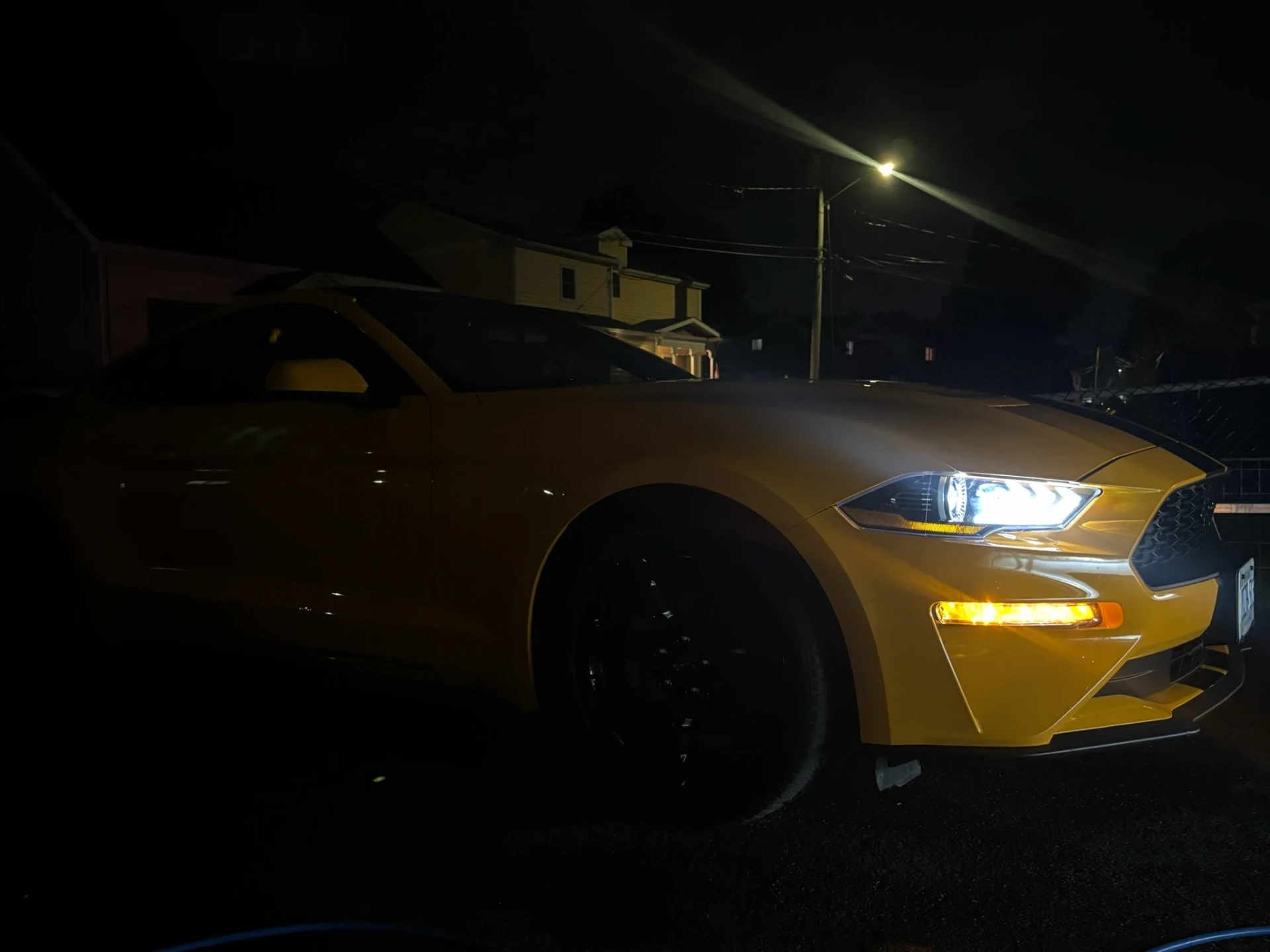 Yellow Ford Mustang with headlights on at night showing glossy paint after an exterior detail