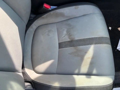 Grey cloth car seat with coffee stains and heavy soiling before shampoo extraction