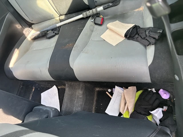 Messy rear seats and floor of a car with trash and stains before an interior deep clean