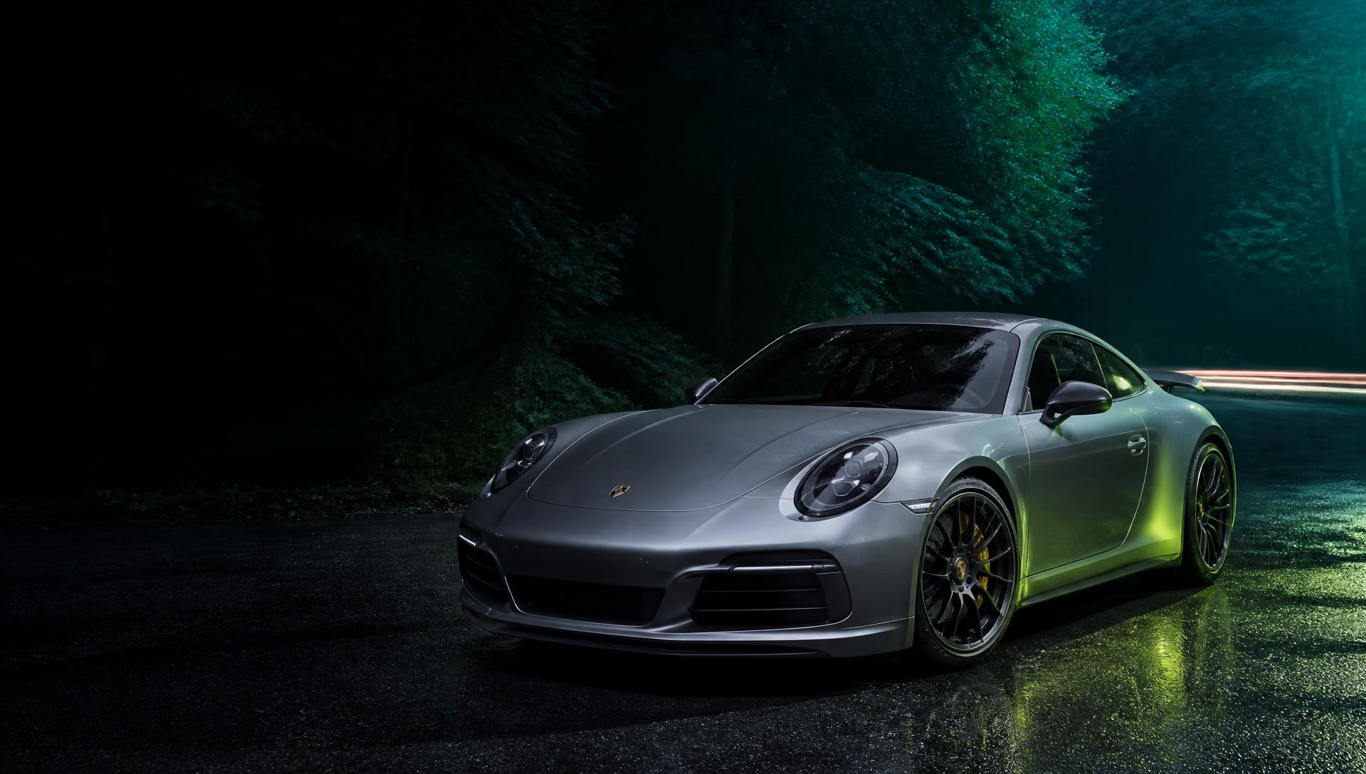 Freshly detailed silver Porsche 911 parked on a wet road at night with green lighting through the trees